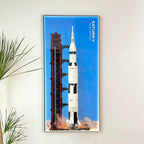 Wall-mounted display frame for LEGO® NASA Apollo Saturn V (21309), shown with rocket model and blue launch backdrop
