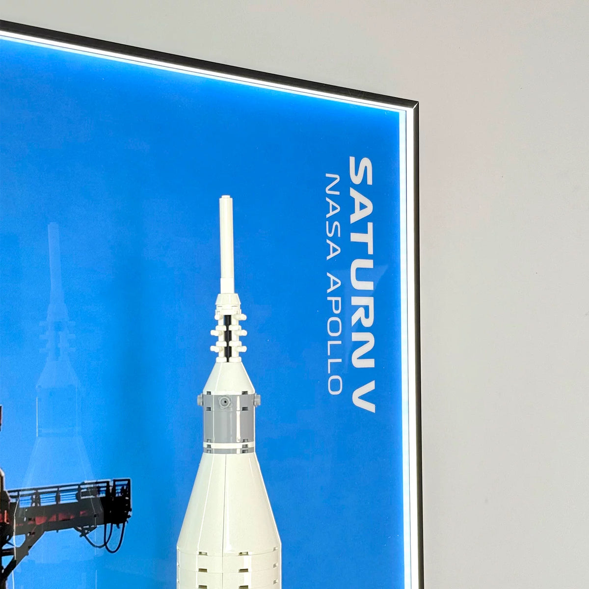 Top detail of wall-mounted display frame for LEGO® NASA Apollo Saturn V (21309), showing illuminated blue backdrop