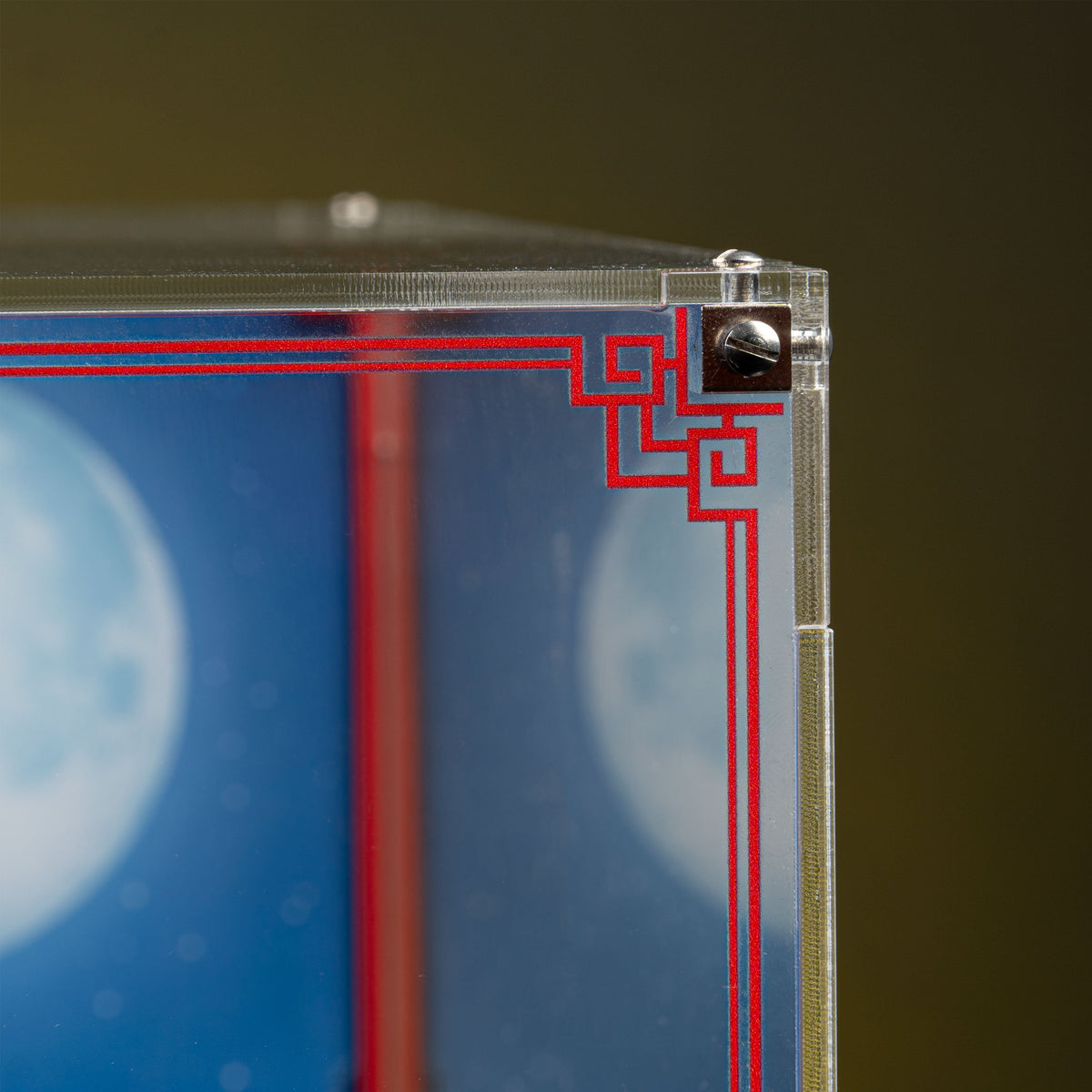 Clear acrylic top-right corner, metal fixing and red decorative border of the LEGO 80121 display case.